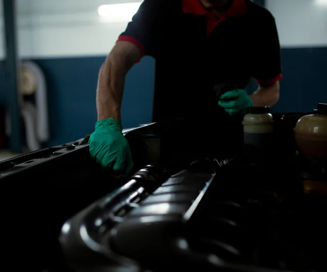 A mechanic in gloves working under an open bonnet