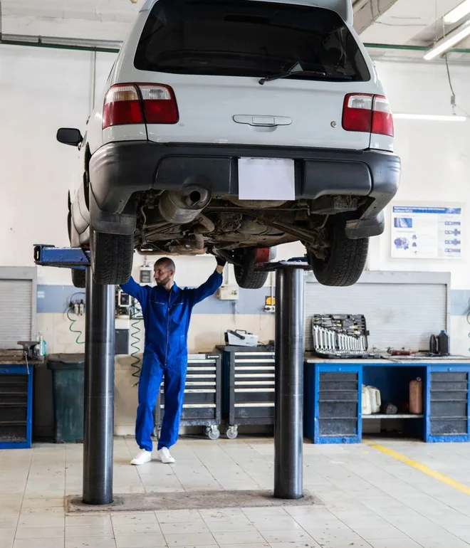 Mechanic in coveralls inspecting a car raised on a lift